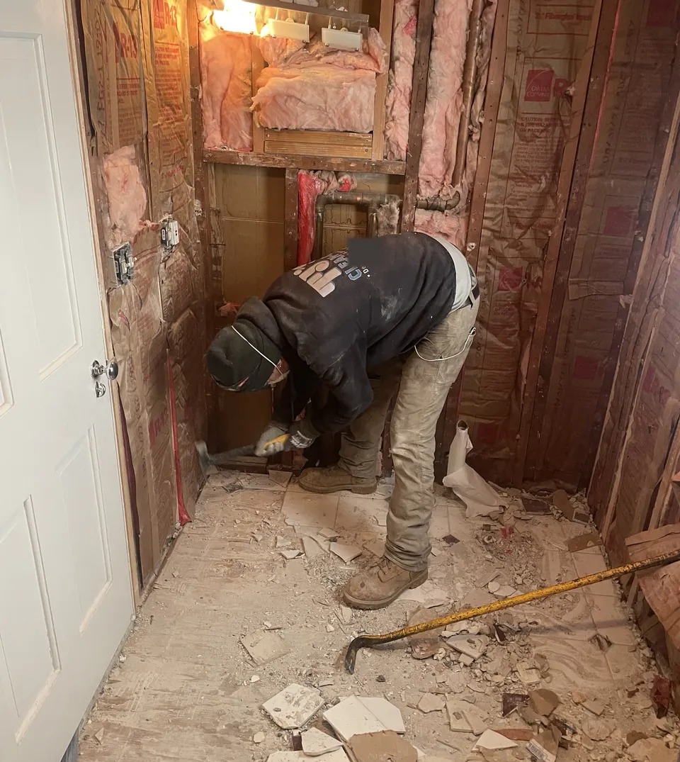 A TJ's crew member tearing out bathroom tile down to the studs
